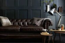 a moody living room with black paneled walls, a dark brown leather sofa and a matching animal skin rug