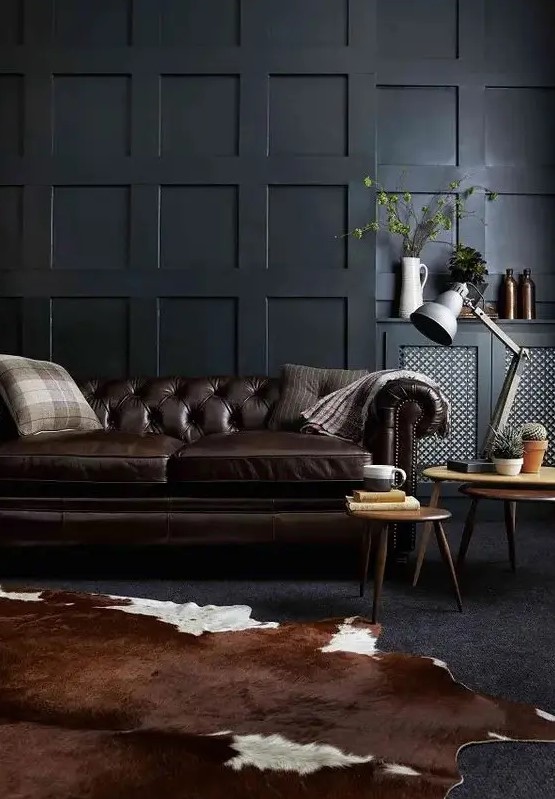 a moody living room with black paneled walls, a dark brown leather sofa and a matching animal skin rug