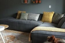 a moody living room with grey walls, a grey low sofa, grey and yellow pillows, a woven chair with faux fur and wire box shelves