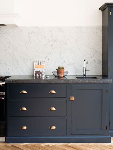 a navy kitchen with flat panel and shaker cabinets, grey soapstone countertops and a white marble backsplash, gold fixtures is wow