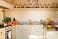 a neutral Provence kitchen with a terracotta tile floor, tan cabinets, a large hood and a white Zellige tile backsplash