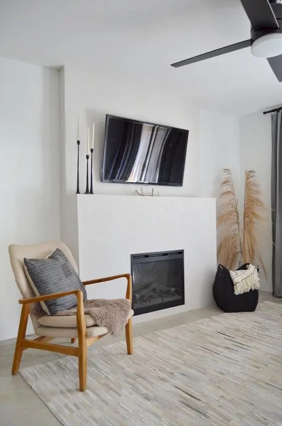 a neutral boho space with a built in fireplace, a TV, pampas grass and a comfy chair with a pillow plus a rug