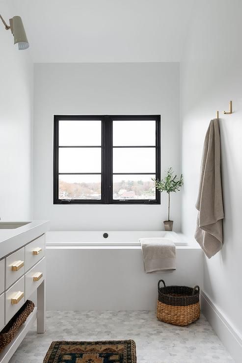 a neutral contemporary bathroom with a black casement window, a neutral console, a built-in bathtub, a marble hex tile floor