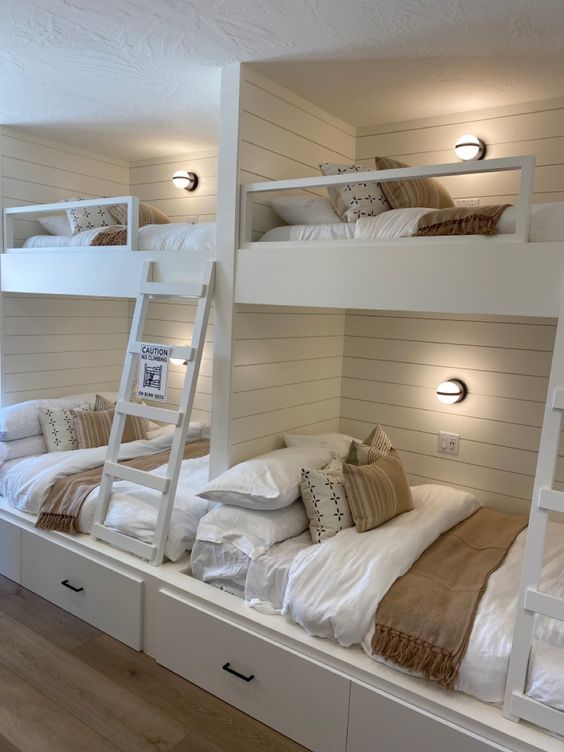 a neutral farmhouse kids' room with multiple bunk beds, neutral bedding and wooden ladders is a cozy space for sleeping