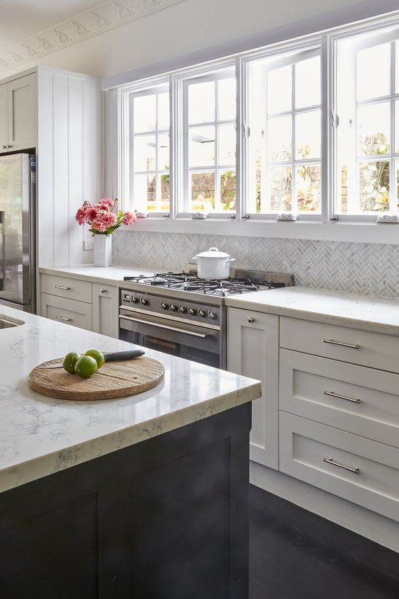 a neutral farmhouse kitchen with shaker cabinets, white stone countertops, casement windows and a black kitchen island