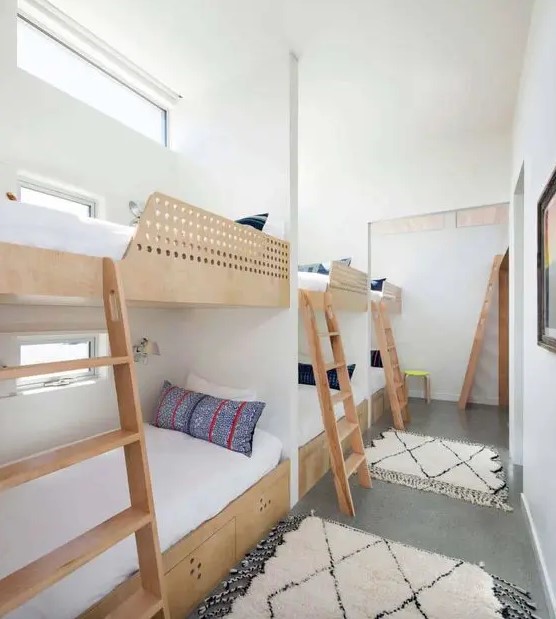 a neutral kids' bedroom with several built in bunk beds with neutral bedding and bright pillows plus ladders