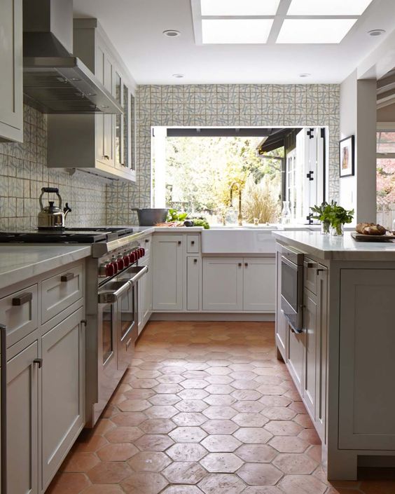 a neutral kitchen with shaker cabinets,  large kitchen island, white stone countertops, a pass through window and a terracotta tile floor