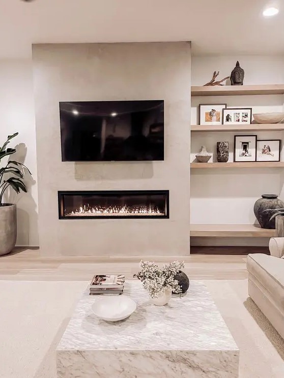 a neutral living room with built in shelves and a fireplace, a marble slab coffee table, a neutral sofa and a potted plant