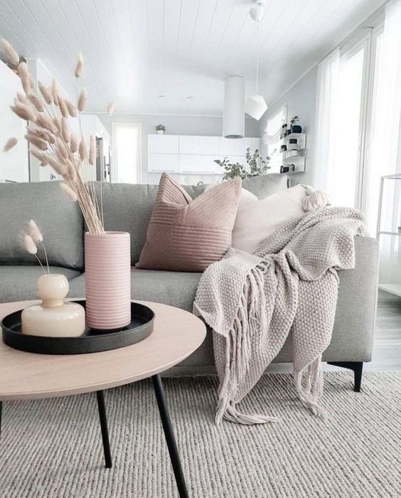 a pretty living room done in grey and blush, with a grey sofa, pink and grey sofas and blankets, a grey rug, a pink vase with dried herbs