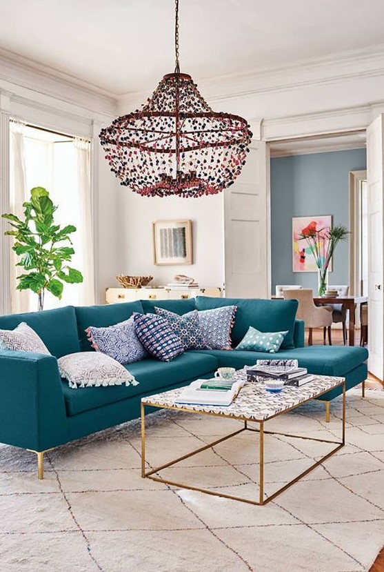 a pretty living room with a turquoise sectional, a cool coffee table, a beaded chandelier and a potted plant plus artworks