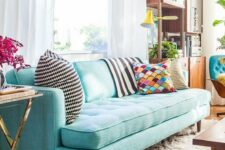 a pretty living room with a turquoise sofa, a modern storage unit, a coffee table and touches of gold here and there