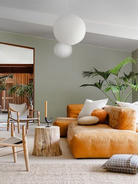 a pretty living room with green walls, a low amber sofa, a tree sutmp, lovely chairs and potted plants
