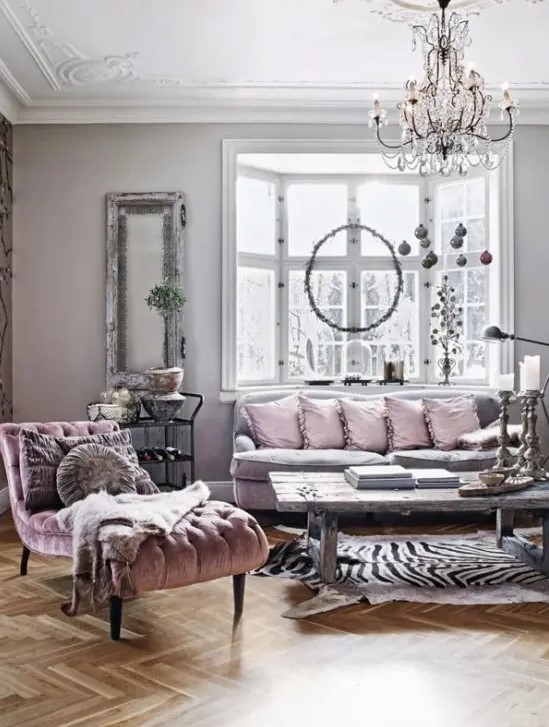 a refined and chic living room with grey walls and a bay window, a grey sofa with pink pillows, a pink lounger and a crystal chandelier