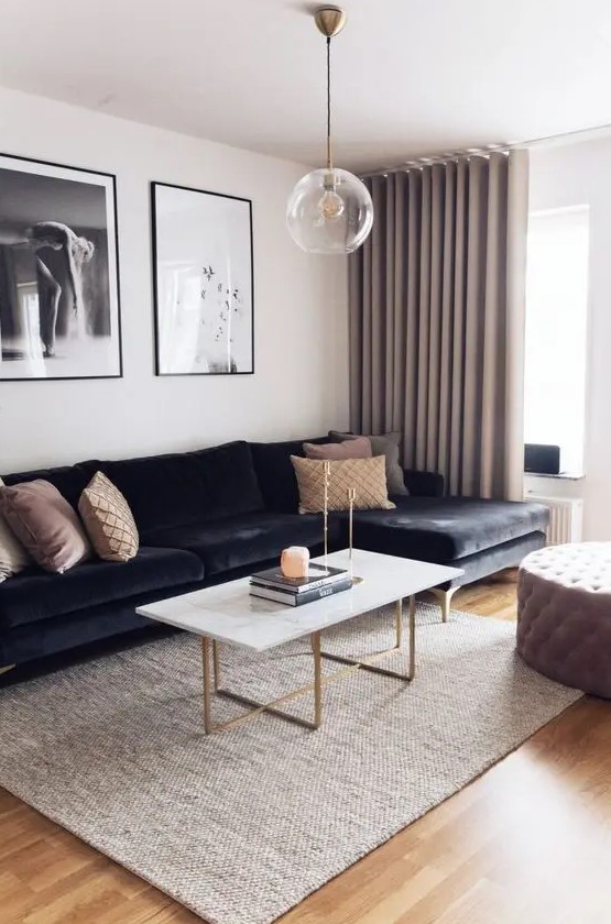 a refined living room with a black sectional, a coffee table with gold legs, a tufted ottoman, a gallery wlal and greige curtains