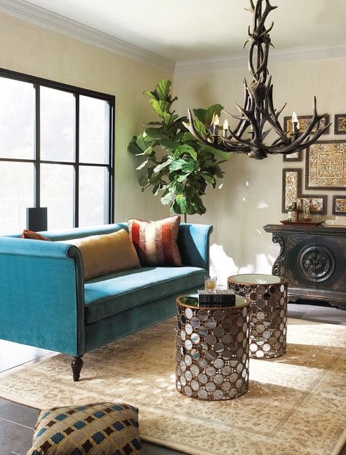 a refined living room with a glazed wall, a turquoise sofa, glass clad coffee tables, an antler chandelier, a refined gallery wall and a statement plant