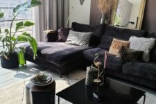 a refined living room with a mauve accent wall, a black sectional, a black coffee table and a side table, layered rugs and printed pillows