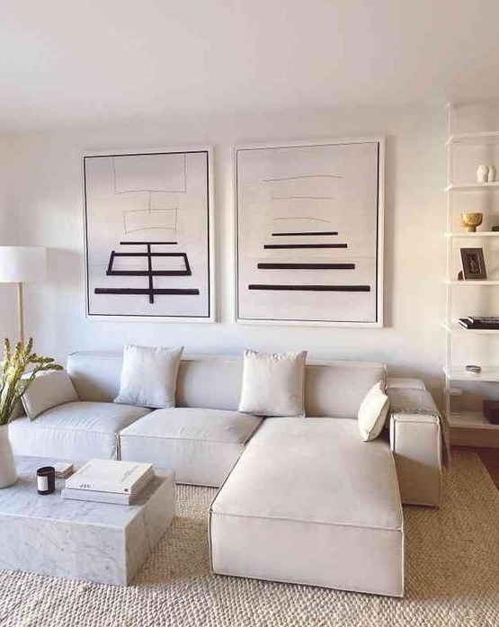 a refined neutral living room with a creamy sectional, a duo of artworks and an open shelving unit, a white marble slab table