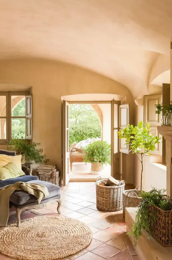 a rustic Spanish style liivng room with terracotta tiles and plaster walls and a ceiling, a refined daybed, baskets and potted plants