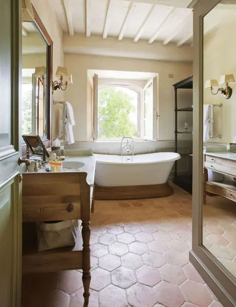 a rustic bathroom with hexagon terracotta tiles, a tub on a wooden stand, a wooden vanity, a wooden table and a large shelving unit
