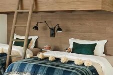 a rustic kids’ room with a wood clad accent wall and bunk beds, printed bedding, black lamps is a very cozy space