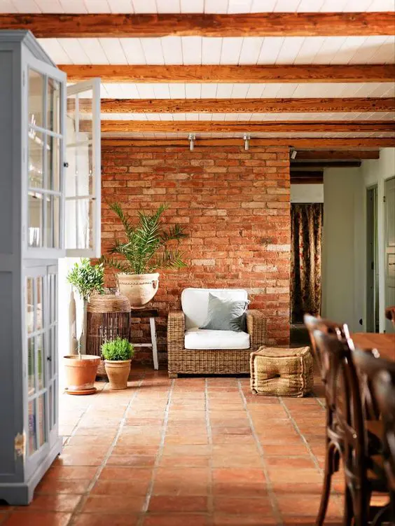 a rustic space clad with brick and terracotta tiles, a woven chair, potted plants and wooden beams on the ceiling