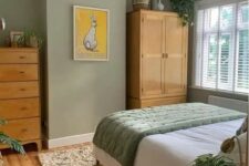 a sage green bedroom with stained furniture, neutral and green bedding, a printed rug and a printed pendant lamp