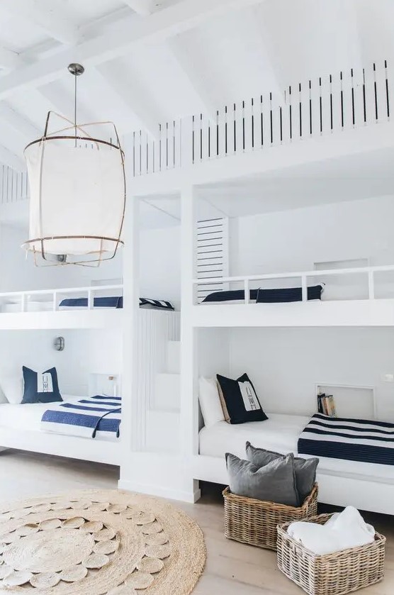 a seaside kids' room with built-in white bunk beds with navy and white bedding, baskets for storage and a woven rug