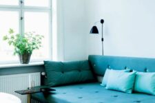 a serene and airy space with a turquoise sofa, a side table, a black lamp and a coffee table plus potted greenery
