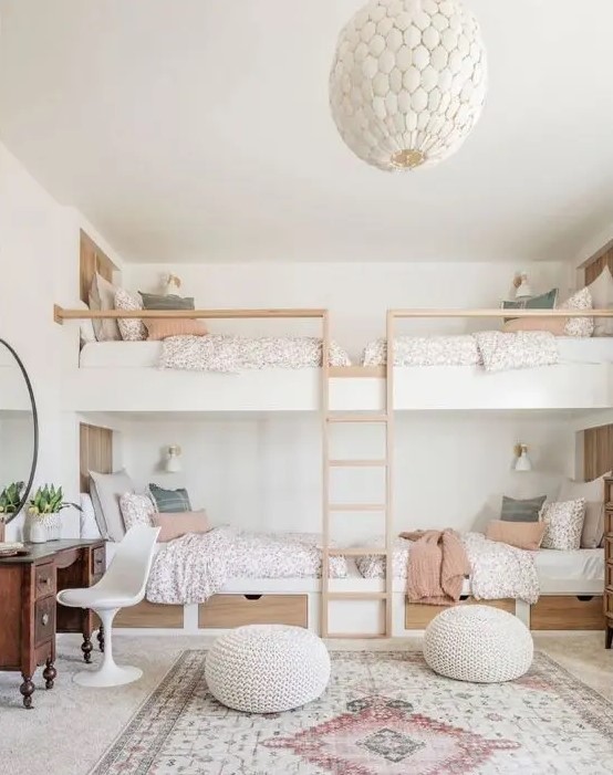 a serene kids' bedroom with built in bunk beds, printed bedding and a rug, poufs, a vintage vanity and a round mirror
