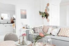 a serene living room with a low grey sofa, a boho printed rug, a grey and a pink pouf, some pink pillows and a carved wooden table