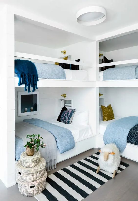 a small and cool coastal kids' room with multiple bunk beds, neutral and printed bedding, a striped rug, woven baskets