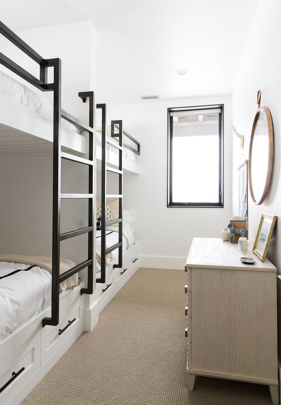 a small and lovely kids' room with multiple bunk beds, blakc ladders, a neutral dresser, a round mirror and a window with a black frame