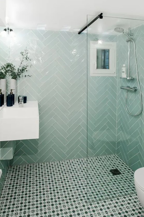a small bathroom with mint herrignbone tiles and printed ones on the floor, a white floating vanity and black touches