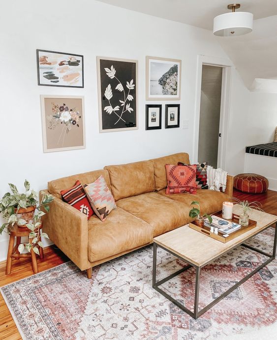 a small boho living room with a tan leather sofa, a coffee table, a gallery wall, a boho printed rug and greenery