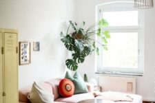 a small bright living room with a yellow locker, a low pink sofa, some potted plants and a catchy pendant lamp
