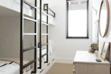 a small neutral kids’ bedroom with built-in bunk beds, black ladders, a large white dresser and a round mirror