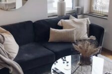 a soft and cozy living room with a black sofa, a clear glass hairpin leg table, neutral pillows and a round mirror