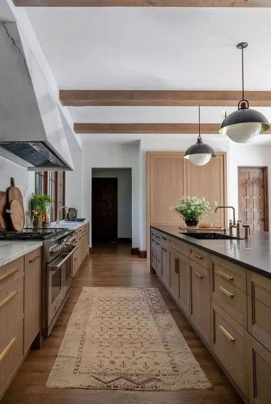 a stained kitchen with shaker cabinets, white marble and black soapstone countertops, wooden beams and hanging lamps