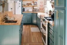 a stylish farmhouse kitchen in teal, with butcherblock countertops, a white backsplash and gold fixtures