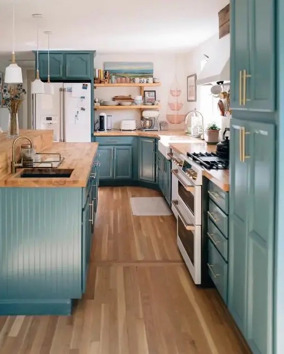 a stylish farmhouse kitchen in teal, with butcherblock countertops, a white backsplash and gold fixtures