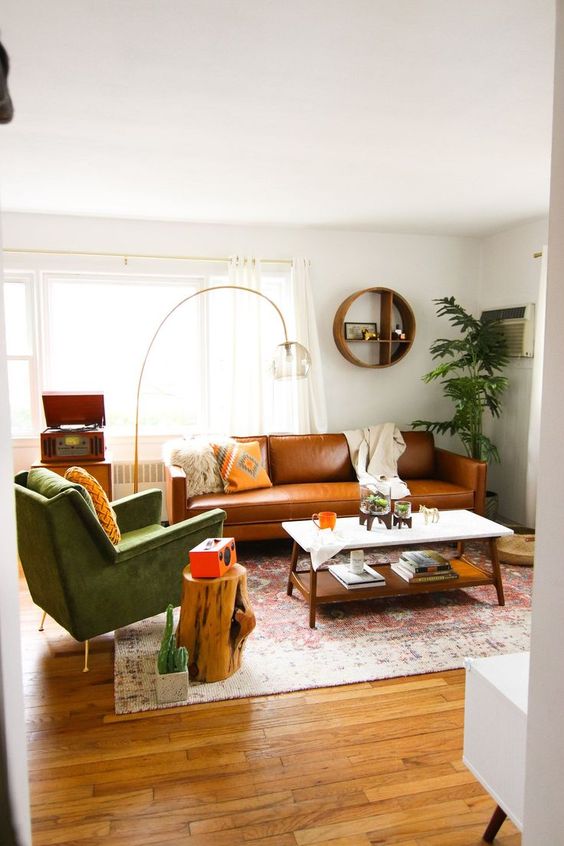 a stylish mid-century modern living room with a tan leather sofa, a green chair, a tiered coffee table and a stump and a floor lamp