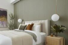 a stylish modern bedroom with a sage green fluted accent wall, a neutral upholstered bed with neutral bedding, rattan nightstands and pendant lamps