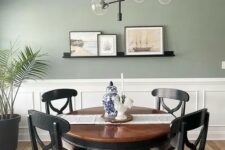 a stylish modern dining room with a sage green wall and paneling, a dark-stained table and chairs, a cool chandelier and some art