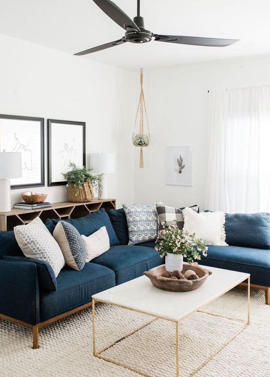 a stylish modern living room with an open storage unit, a navy sectional, a coffee table, potted greenery and blooms