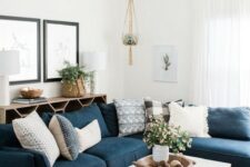 a stylish modern living room with an open storage unit, a navy sectional, a coffee table, potted greenery and blooms