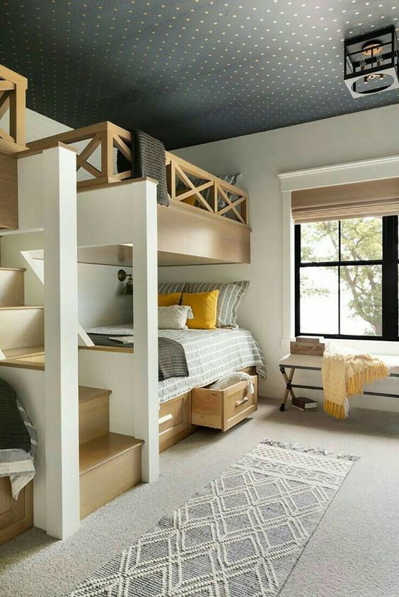 a stylish modern rustic kids' room with multiple bunk beds with storage drawers, an upholstered bench, a printed rug and bedding