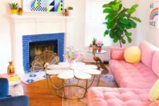 a vibrant living room with a fireplace clad with blue tiles, a pink sectional, a blue chair, a glass and a brass coffee table and a bold artwork