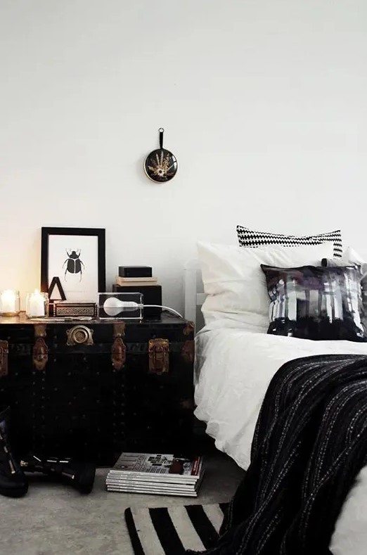 a vintage black trunk with copper detailing serves as a nightstand and a storage piece and it looks amazing
