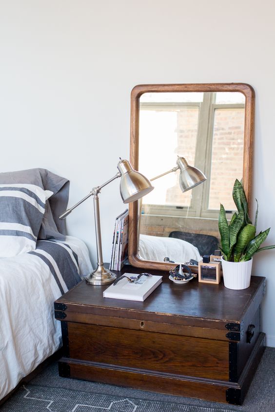 a vintage dark-stained chest with no detailing, with a mirror, a potted plant and a shiny metal lamp is a lovely space