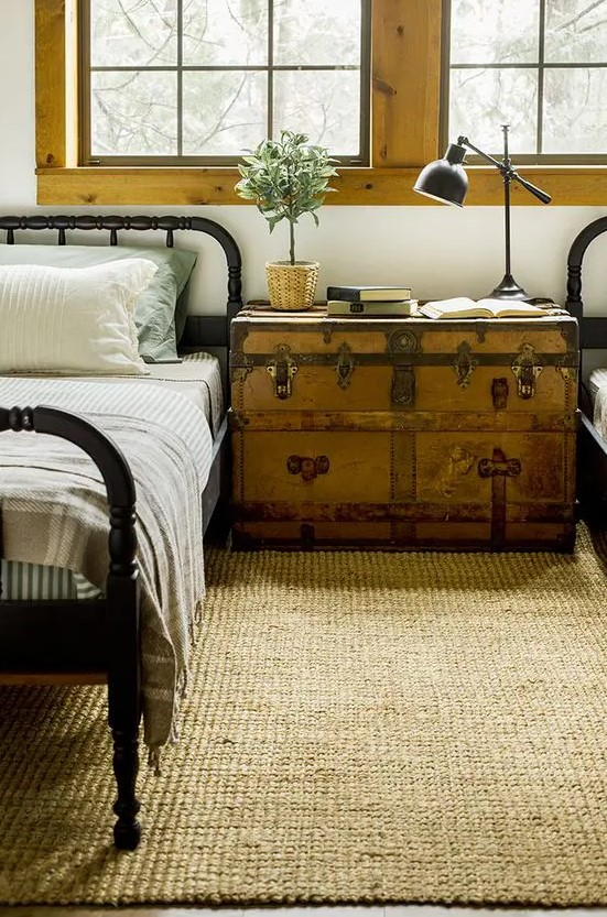 a vintage farmhouse guest bedroom with a large window, black beds, a vintage trunk as a shared nightstand and a black lamp